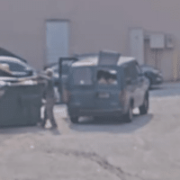 A man begins taking personal trash out of the van and placing it into the private dumpster.