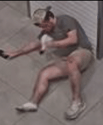 The injured male is laying on the floor of the elevator, holding his phone in his right hand and his right shoe in his left hand.
