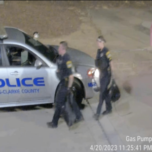 Two police officers carry the suspects' belongings off of the property.